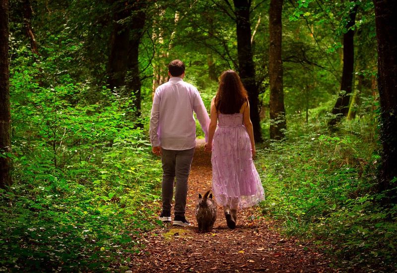 two female figures stand facing each other in front of a stone wall and natue backdrop